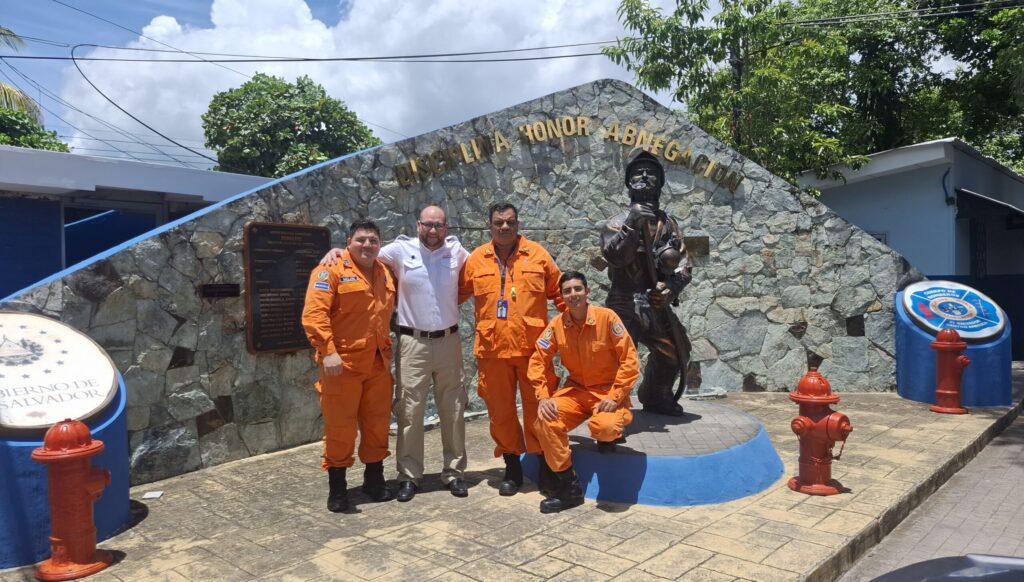 Claudio Sáez con bomberos de El Salvador frente a monumento para bomberos